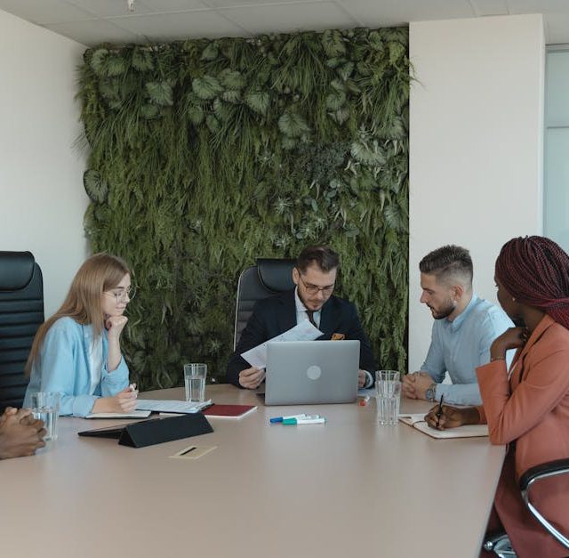 A diverse team brainstorms in a modern office with green wall decor.